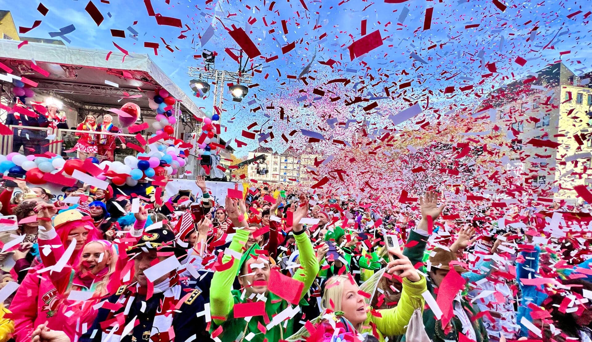 Das Foto zeigt feiernde Jecken im Karneval, die im Konfettiregen stehen.