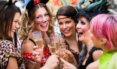 Fünf kostümierte Frauen feiern Karneval und stoßen dabei mit Sekt an.