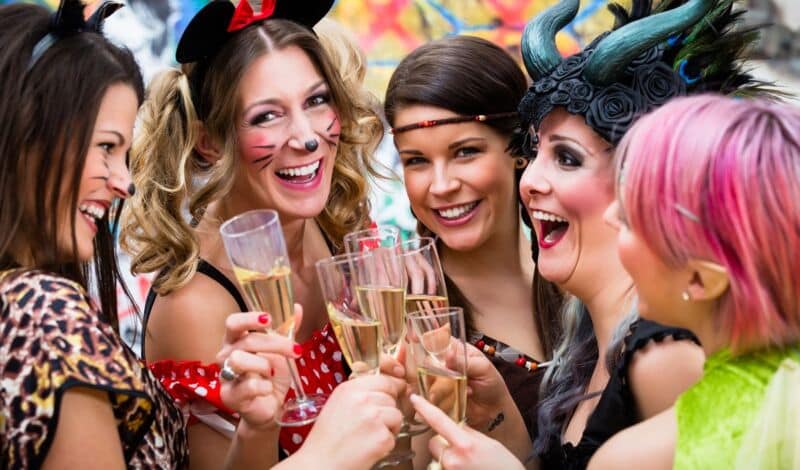 Fünf kostümierte Frauen feiern Karneval und stoßen dabei mit Sekt an.