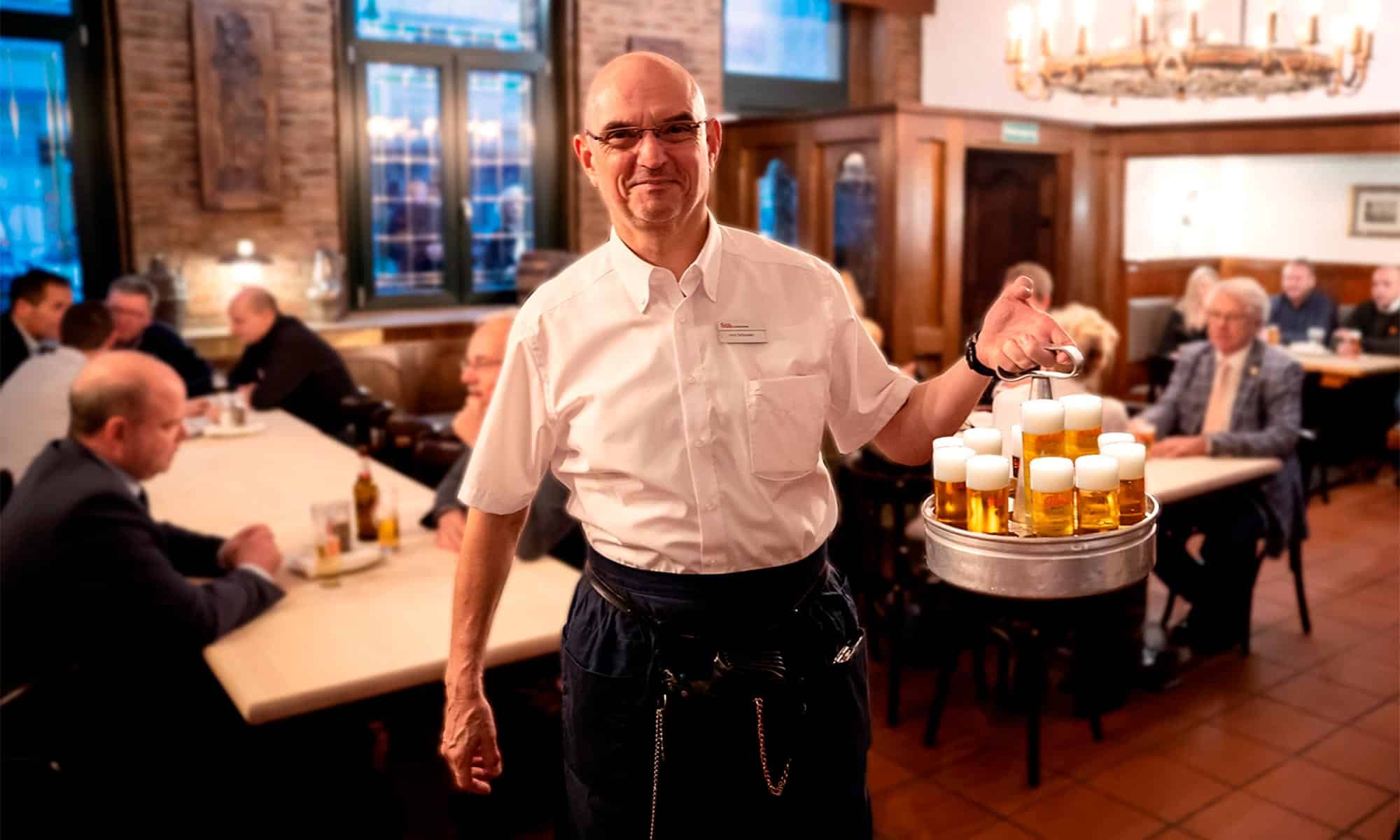 Köbes im Brauhaus mit einem Kranz Kölsch
