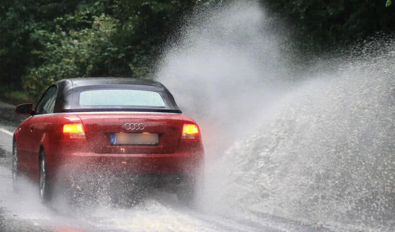 Ein Auto fährt durch eine von Starkregen überflutete Straße.