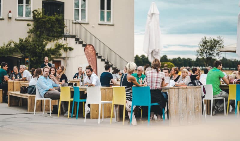 Besucher des Weinfests am Rhein sitzen gemütlich an Tischen im Rheinauhafen.