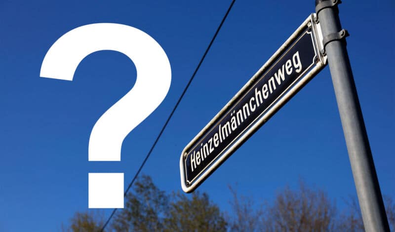 Ein Straßenschild mit der Beschriftung Heinzelmännchenweg sowie ein Fragezeichen vor blauem Himmel.