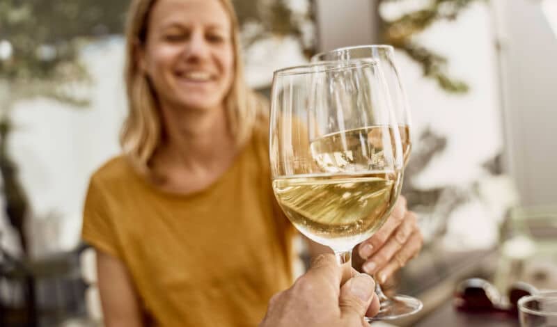 Frau stößt mit einem Glas Weißwein an.