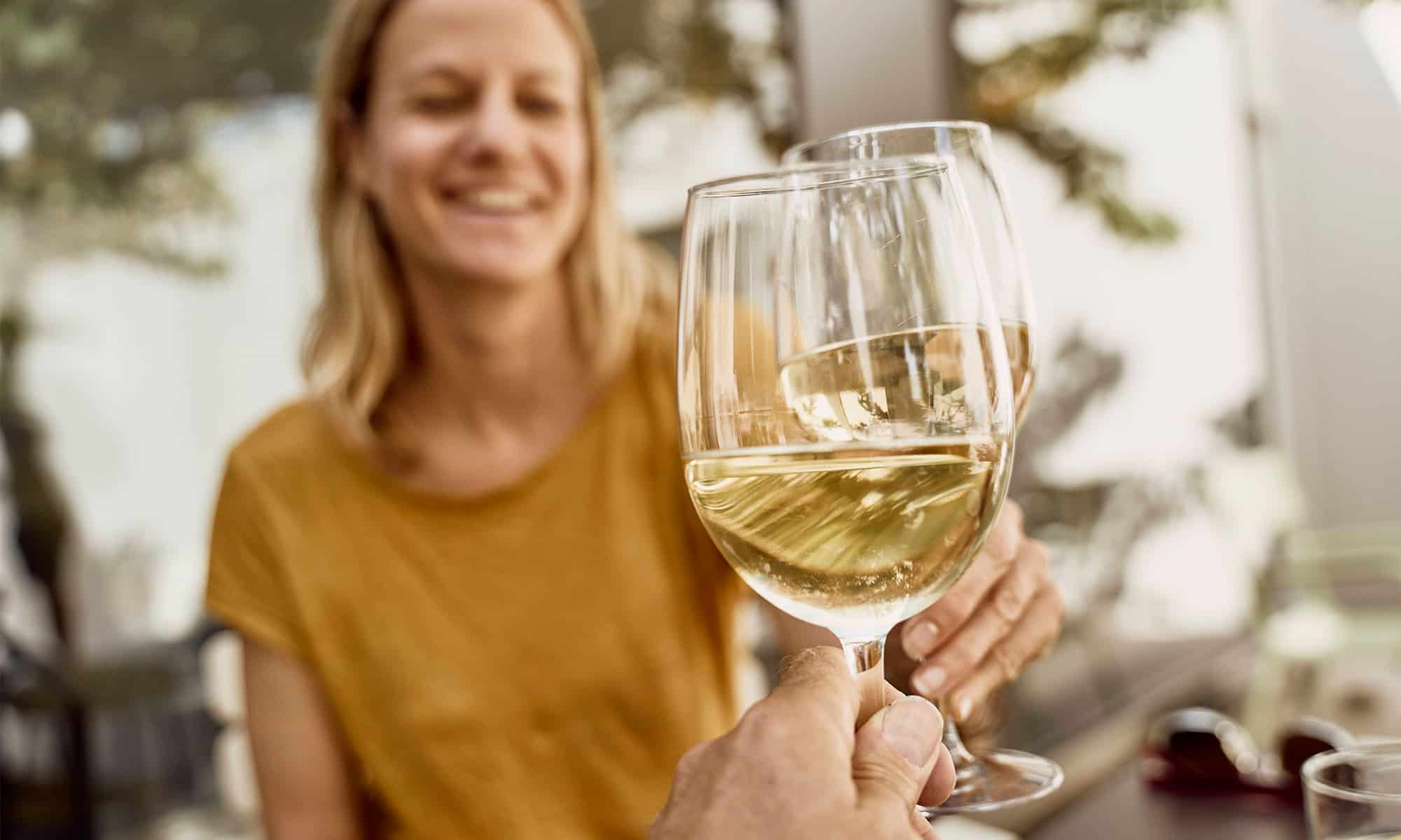 Frau stößt mit einem Glas Weißwein an.