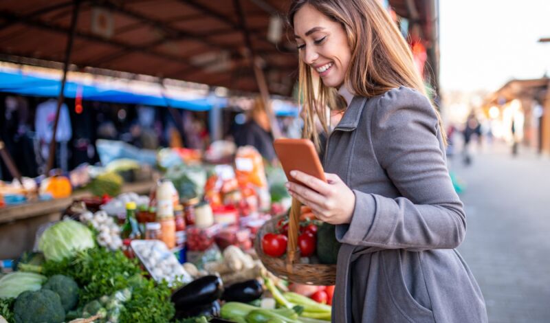 Frau mit Handy vor Gemüsestand