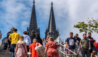 Menschen gehen auf einer Treppe mit den Türmen des Kölner Doms im Hintergrund