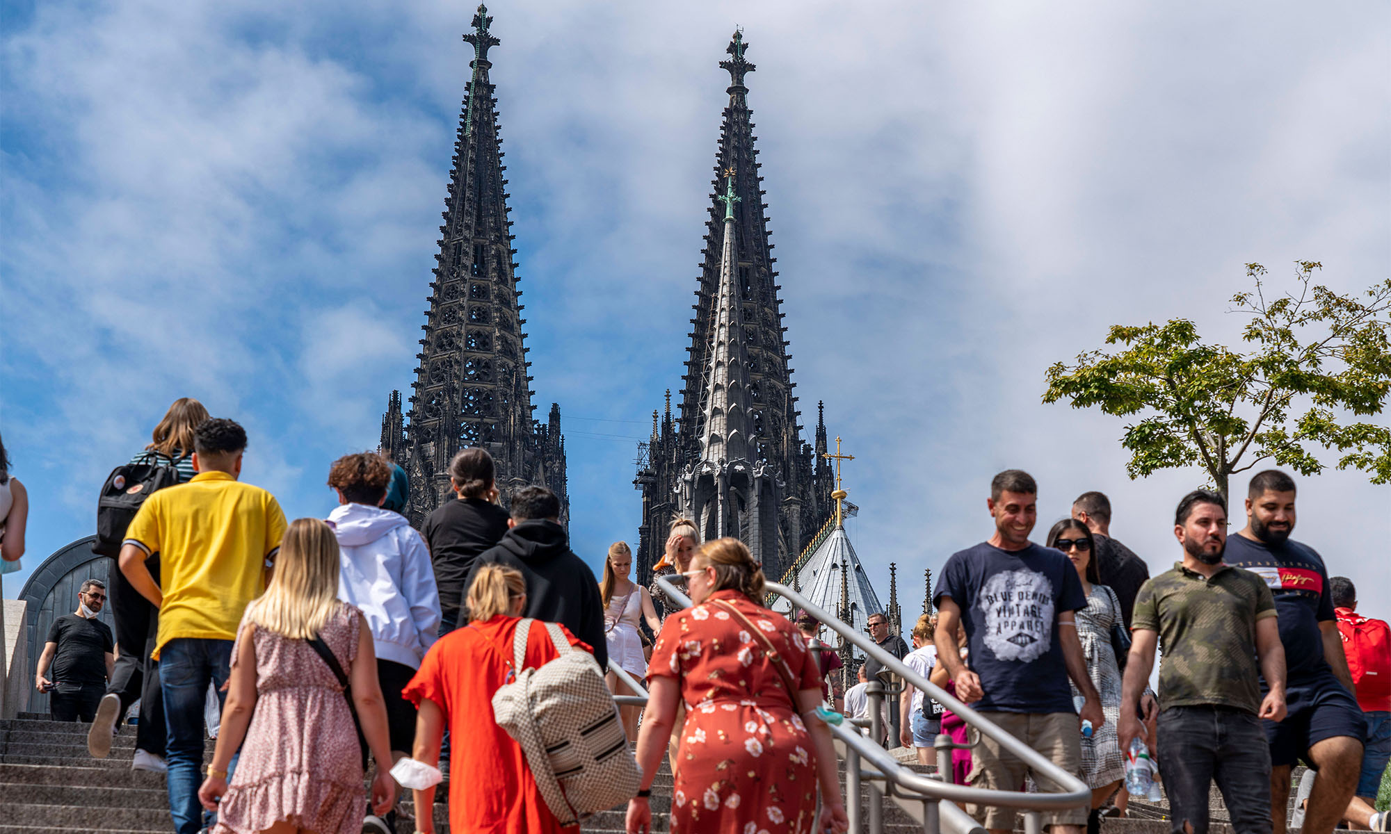 Menschen gehen auf einer Treppe mit den Türmen des Kölner Doms im Hintergrund