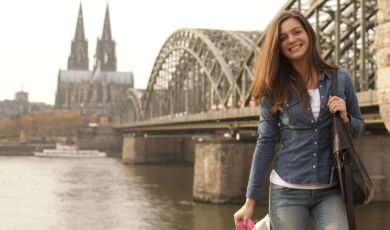 Frau mit Einkaufstasche posiert vor Kölner Dom und Hohenzollernbrücke