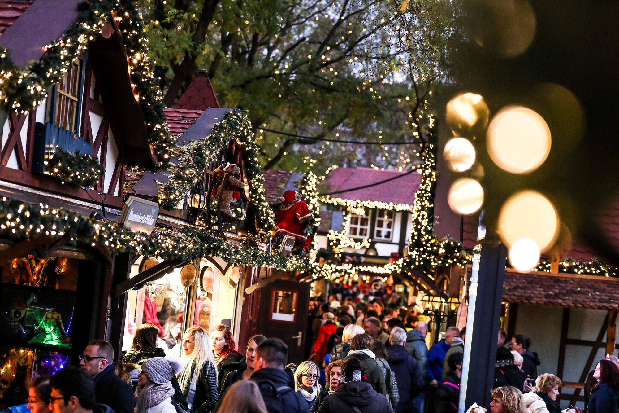 Das Foto zeigt Menschen zwischen hell erleuchteten Fachwerkhäuschen auf dem Nikolausdorf Weihnachtsmarkt in Köln.