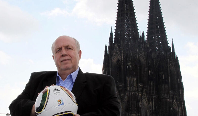 Das Foto zeigt Reiner Callmund mit einem Fußball in der Hand vor der Kulisse des Kölner Doms.