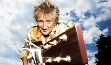 Der Britische Sänger Rod Stewart hält ein Gitarre nach vorne von sich weg.