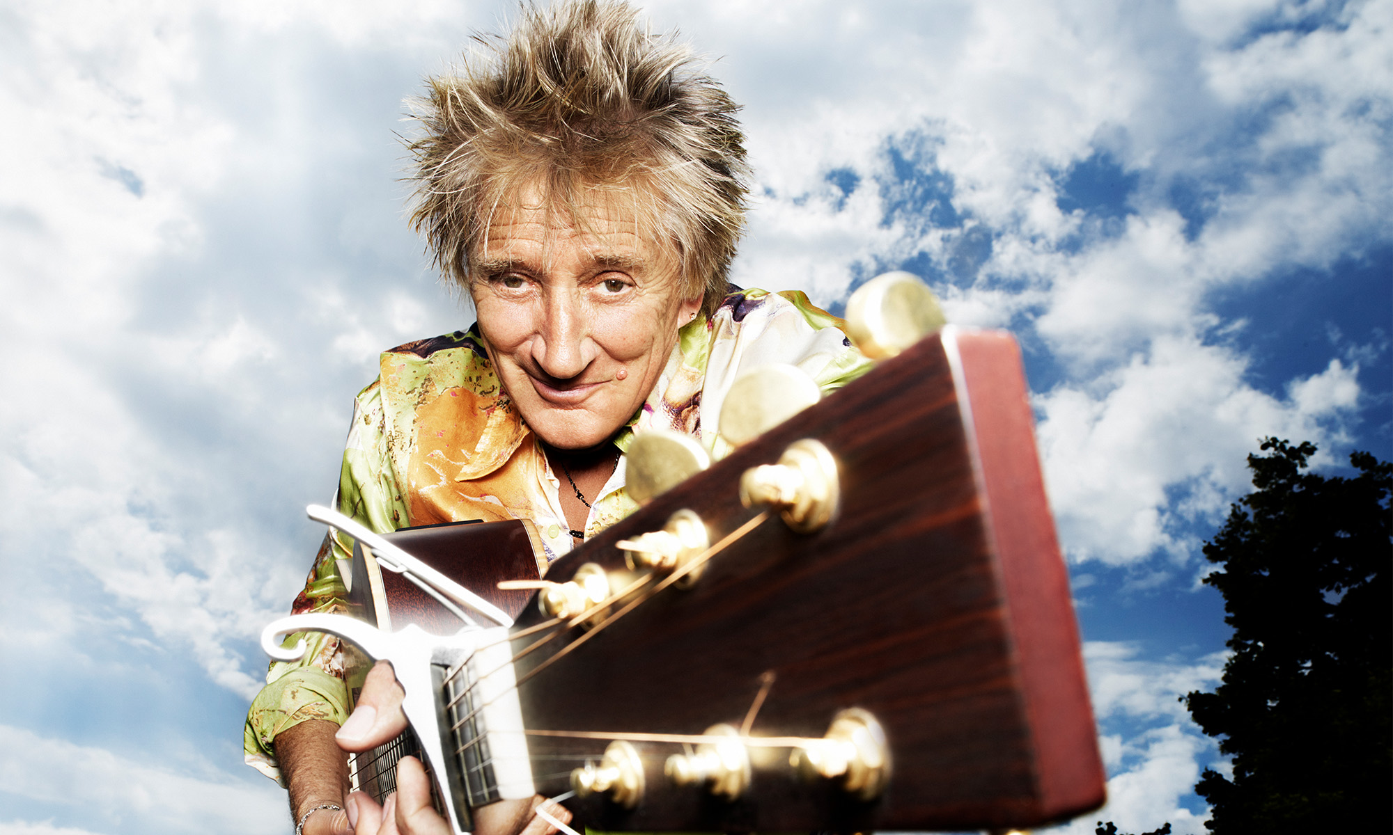 Der Britische Sänger Rod Stewart hält ein Gitarre nach vorne von sich weg.