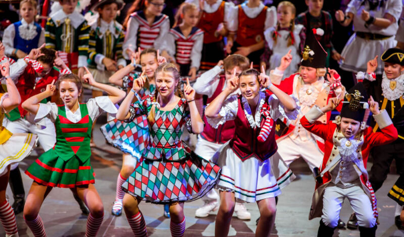 Das Foto zeigt verkleidete, tanzende Kinder bei der Lachenden Pänzarena auf der Bühne der Kölner Lanxess-Arena.