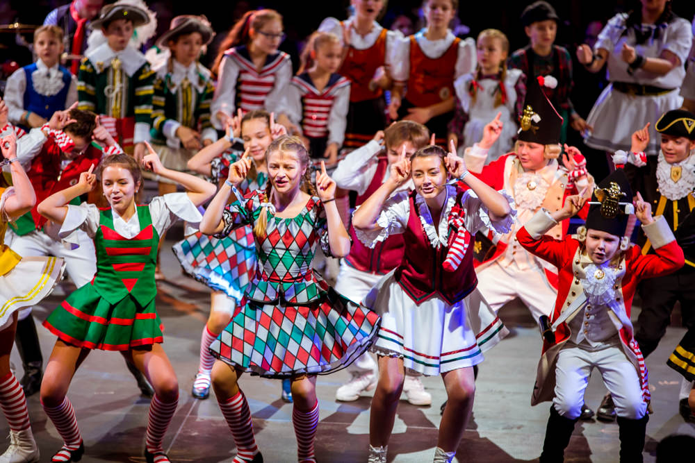 Das Foto zeigt verkleidete, tanzende Kinder bei der Lachenden Pänzarena auf der Bühne der Kölner Lanxess-Arena.