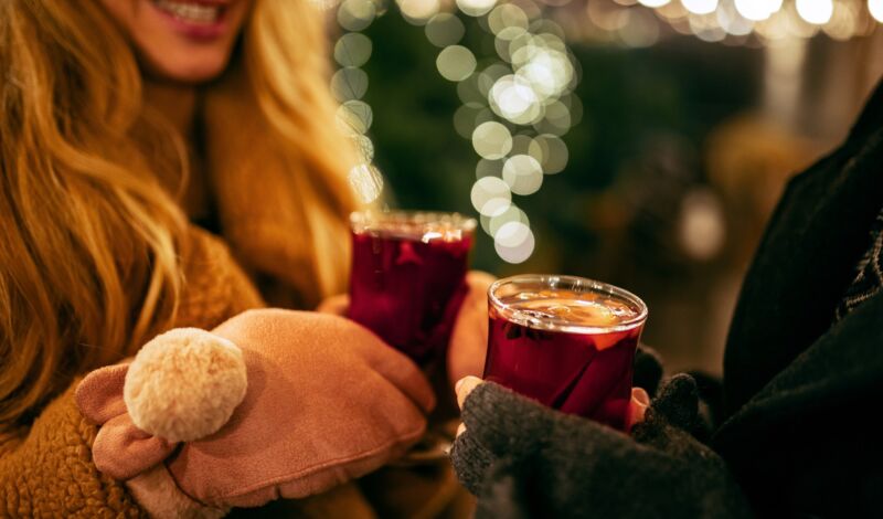 Zwei Personen stoßen mit Glühwein an auf Weihnachtsmarkt