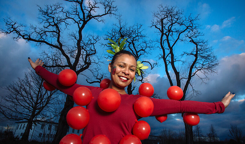 Junge Frau posiert in selbstgemachten Erdbeer-Kostüm aus roten Luftballons.