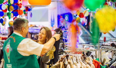Frau lässt sich beim Kauf eines Karnevalskostüms beraten und lacht dabei herzlich.