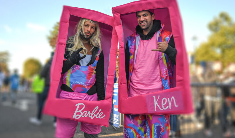 Zwei Männer kostümiert als Barbie und Ken in einer Verpackung.