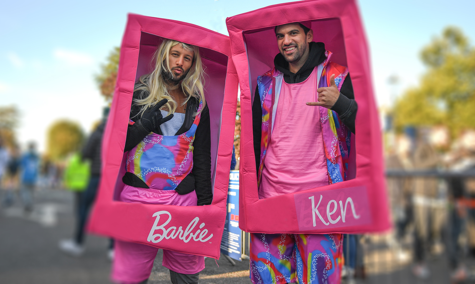 Zwei Männer kostümiert als Barbie und Ken in einer Verpackung.