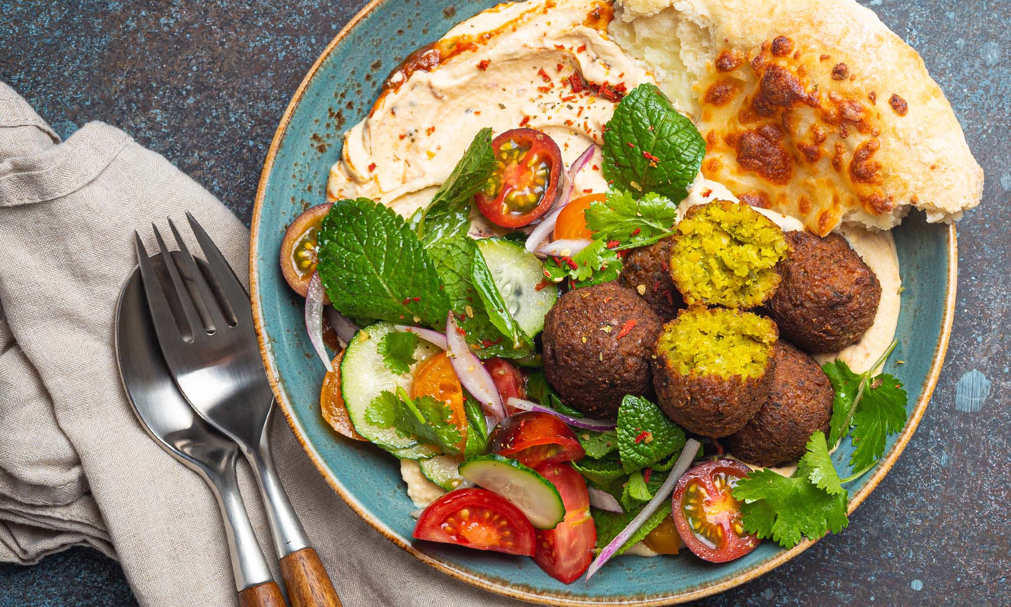Falafelbällchen mit Salat zusammen mit Hummus und einem Fladenbrot auf einem Teller