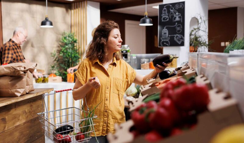 Eine Frau kauft in einem Hofladen Obst und Gemüse ein.