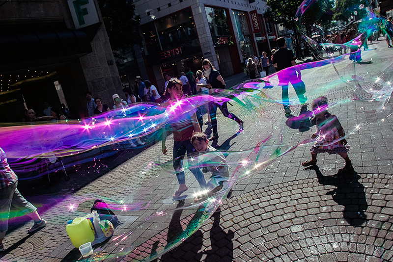 Seifenblasen eines Straßenkünstlers schweben über den Köpfen von Kindern auf der Schildergasse in Köln.