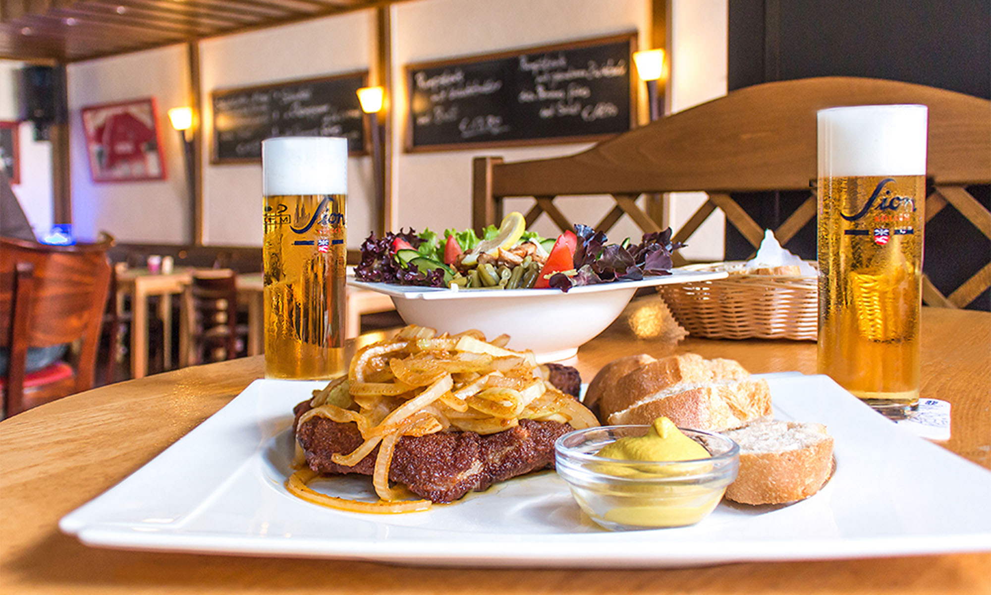Zwei Gläser Kölsch und ein Steak auf einem Teller in einer Gaststätte.