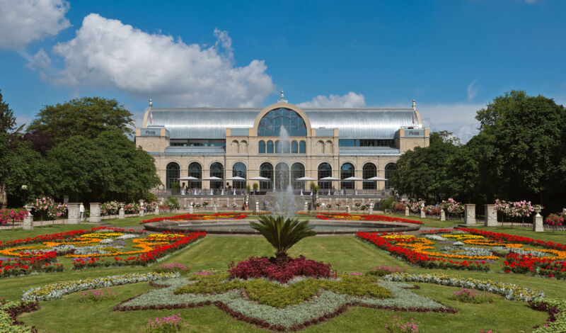 Blumenreicher Botanischer Garten und Park mit dem Gebäude der Flora im Hintergrund.