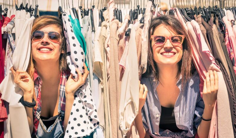 Zwei junge Frauen gucken zwischen Kleiderständern mit Mode hervor