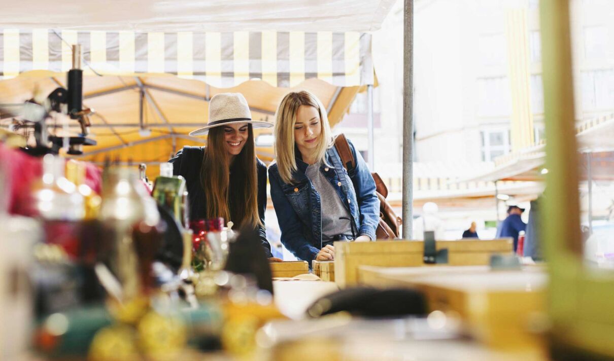 Zwei junge Frauen schlendern über einen Flohmarkt