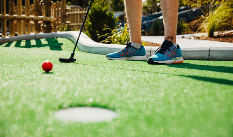 Man sieht die Beine eines Mannes, der Minigolf spielt.