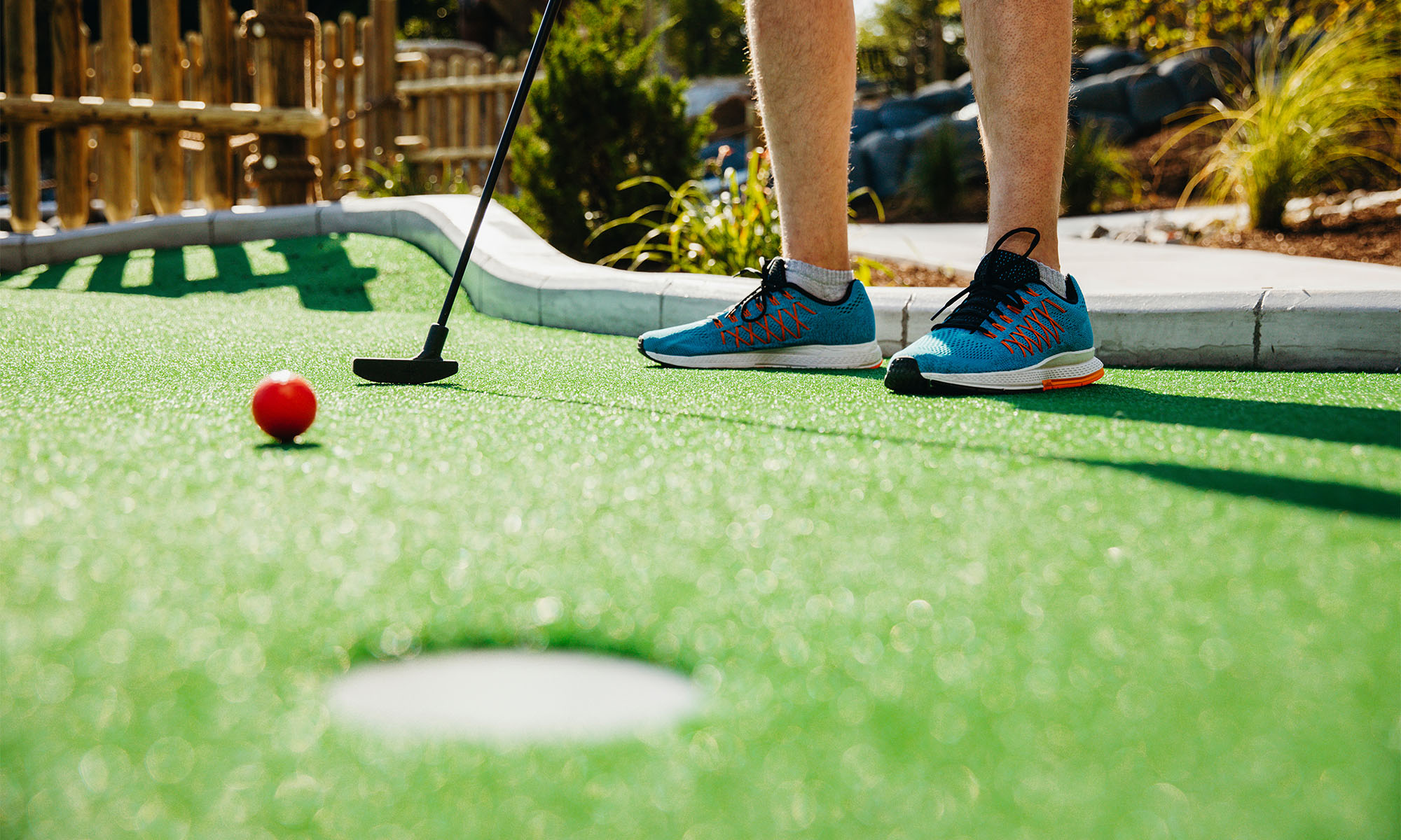 Man sieht die Beine eines Mannes, der Minigolf spielt.
