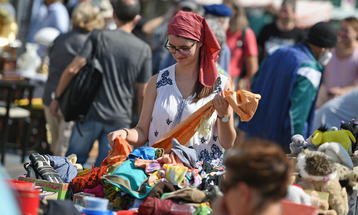 Frau stöbert auf einem Flohmarkt in einem Haufen Second-Hand-Bekleidung.