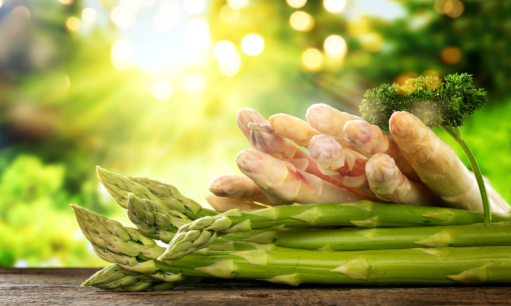 Grüner und weißer Sparge liegen auf einer Holzplatte im Gegenlicht.