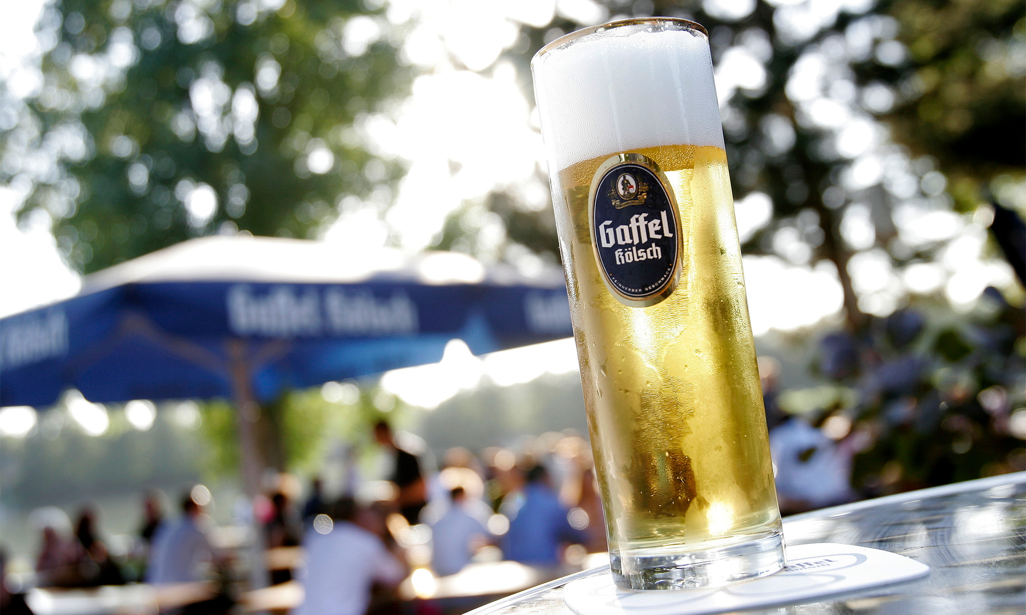 Ein Glas Kölsch von Gaffel, im Hintergrund der Biergarten am Aachener Weiher