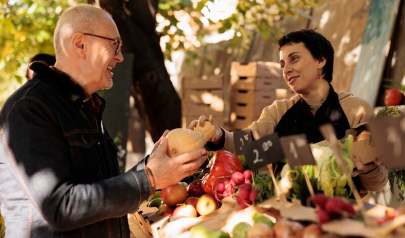 Ein älterer Herr kauft draußen in einem Bauernladen ein