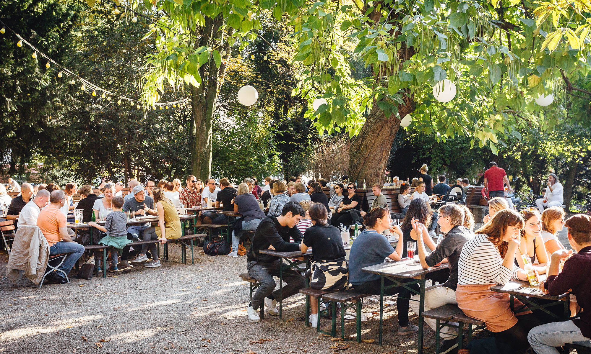 Besucher sitzen an Biertischen im Biergarten Stadtgarten