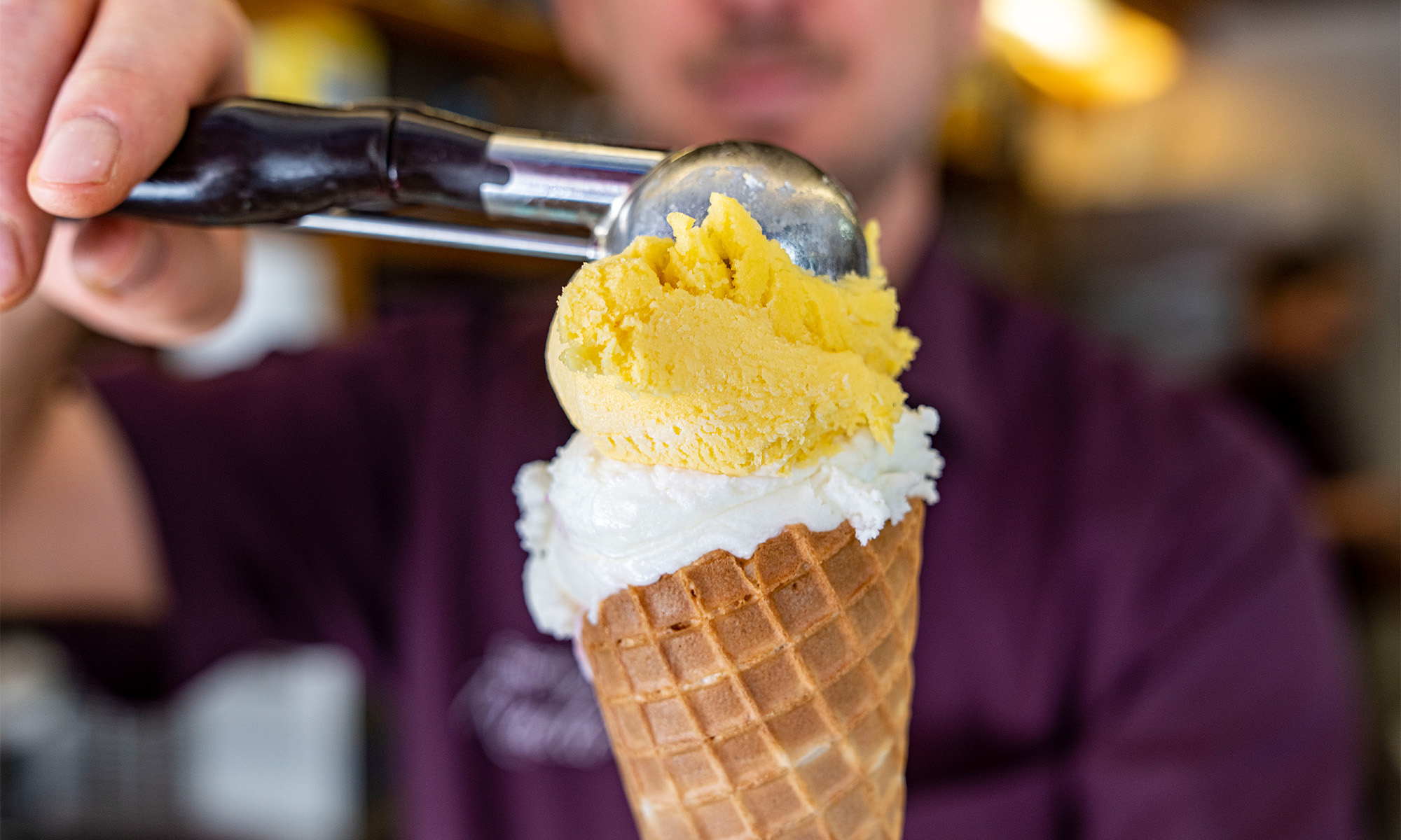 Mit einem Eisportionierer setzt ein Eisverkäufer eine Kugel Eiscreme auf eine Waffel.