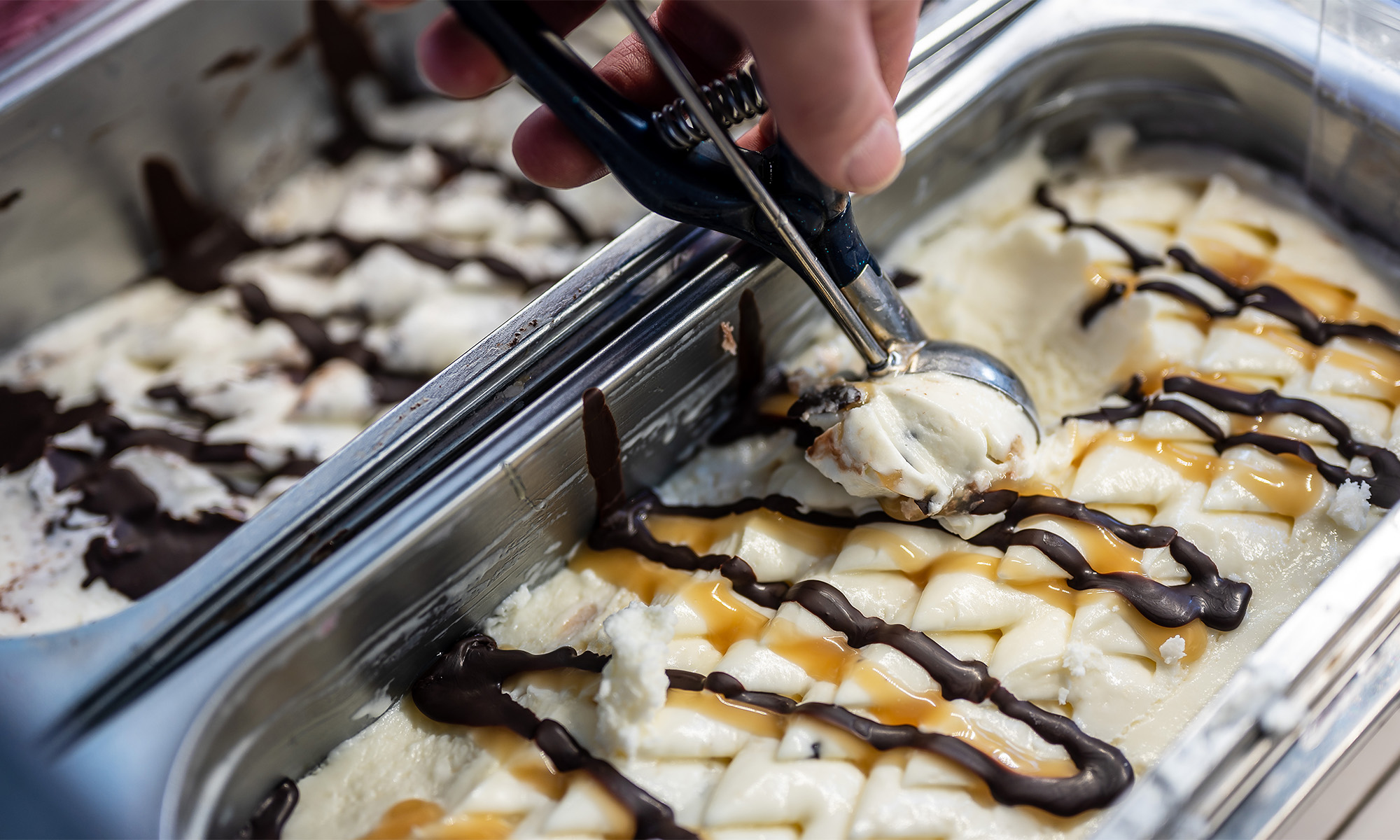 Ein Eisverkäufer holt mit einem Portionierer eine Kugel Eis aus der Kühltheke.