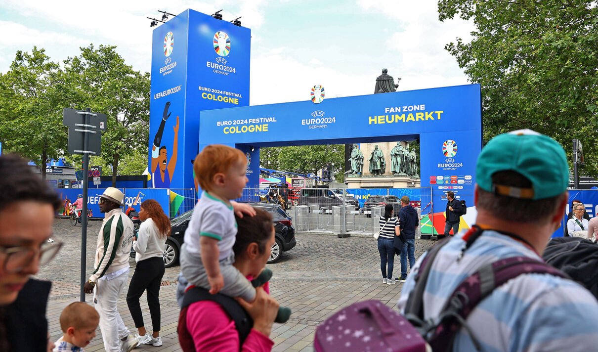 Passanten am Eingang der Fan Zone der EURO 2024 auf dem Kölner Heumarkt.
