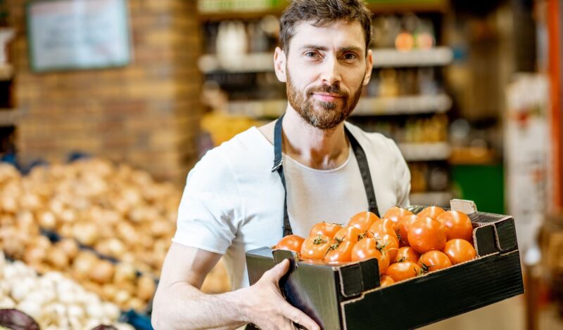 Mann trägt karton voller Tomaten durch ein Geschäft