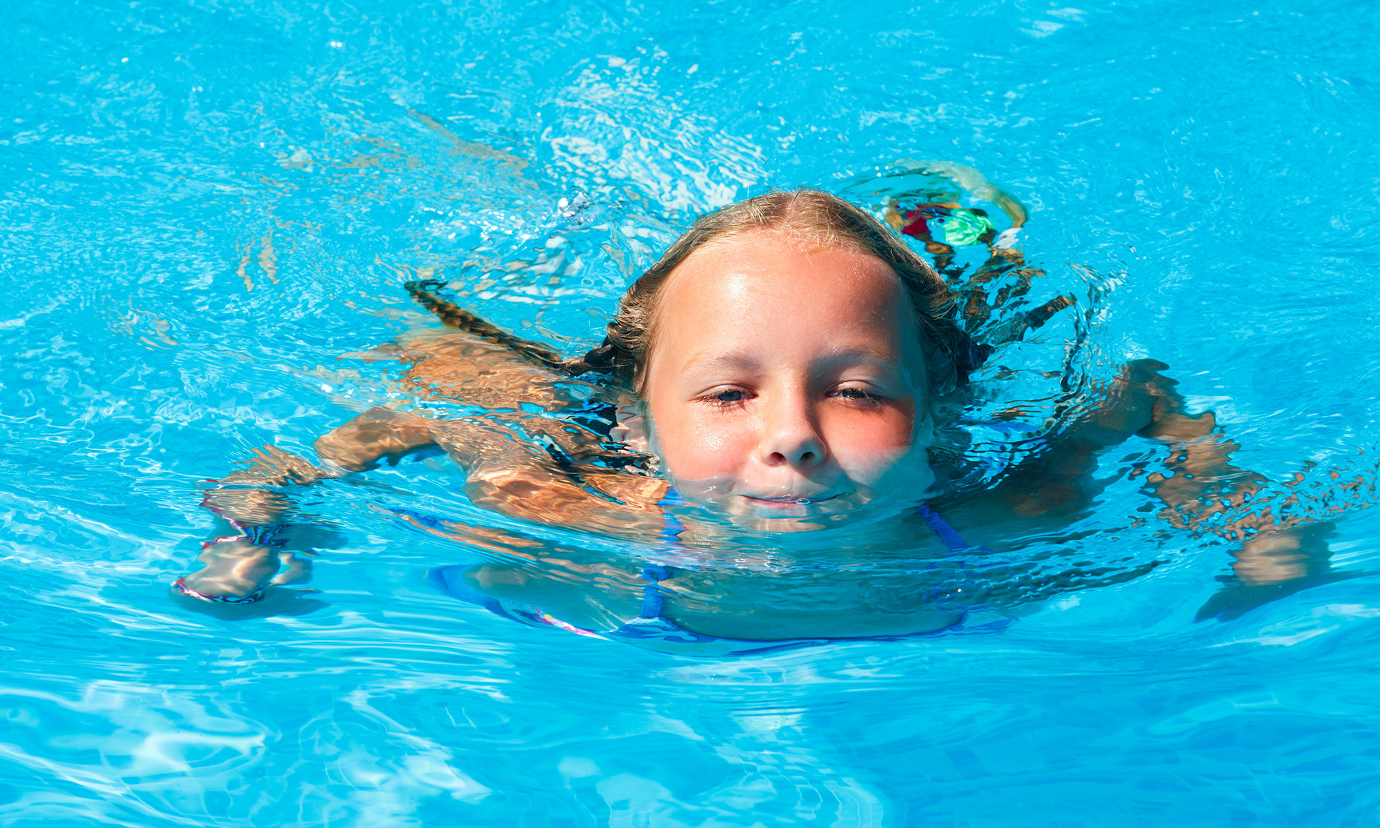 Mehrere Personen schwimmen auf einer Luftmatratze im Fühlinger see, im Hintergrund der Sandstrand
