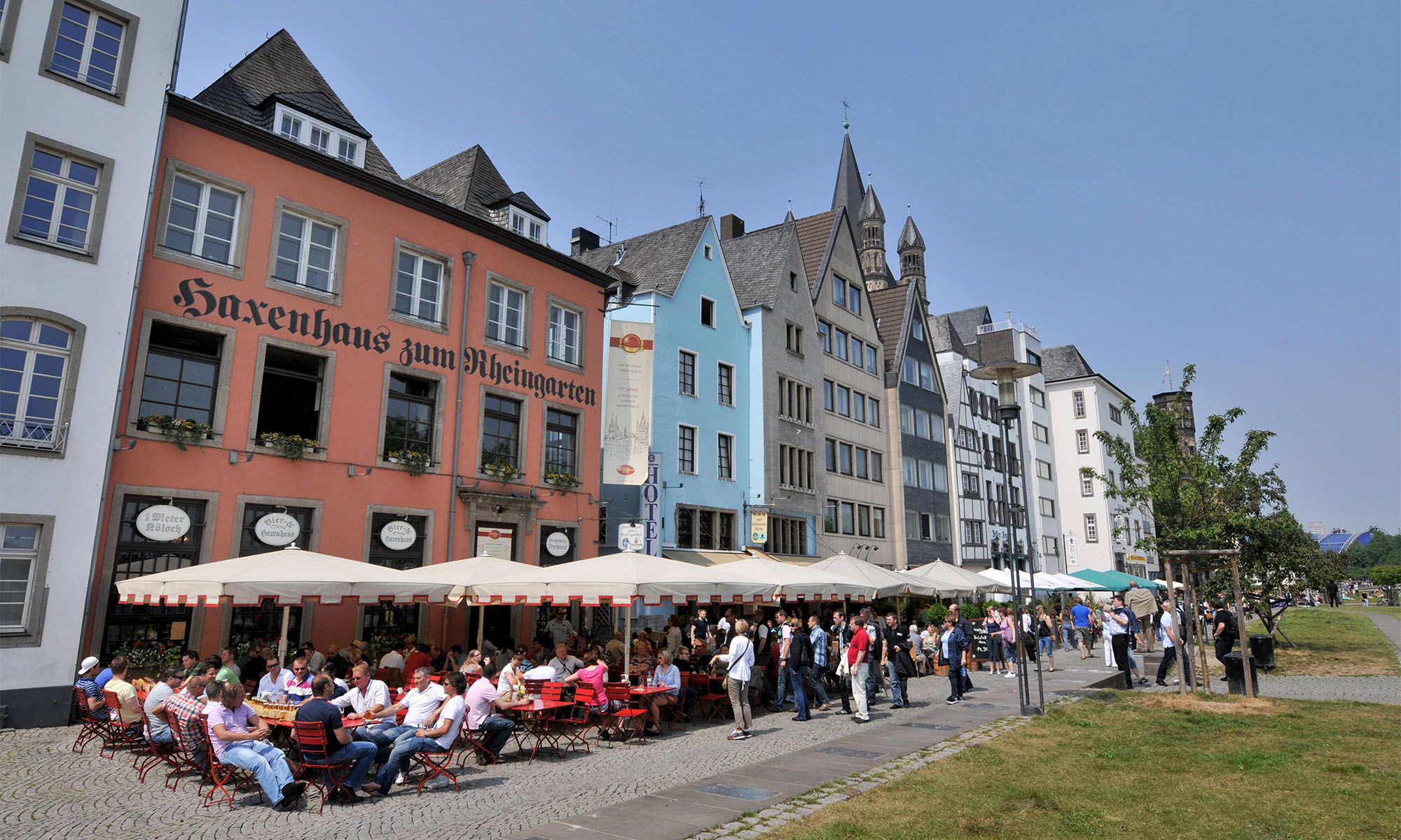 In der Außengastronomie der Lokale am Kölner Rheingarten sitzen Gäste unter Sonnenschirmen