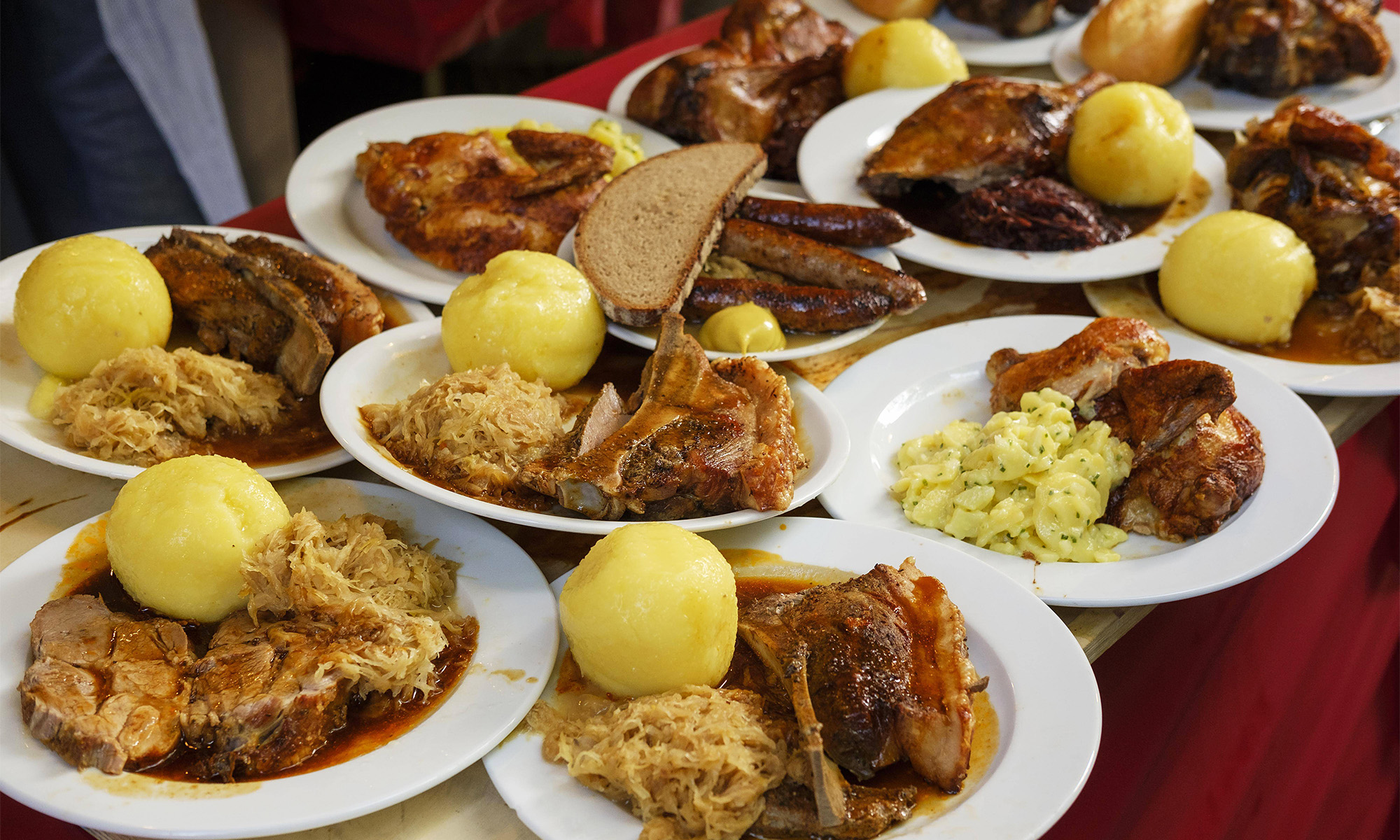 Mehrere Teller mit Kotelett und Schweinebraten samt Sauerkraut und Kartoffelkloß