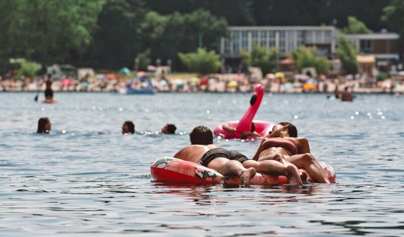 Mehrere Personen schwimmen auf einer Luftmatratze im Fühlinger see, im Hintergrund der Sandstrand