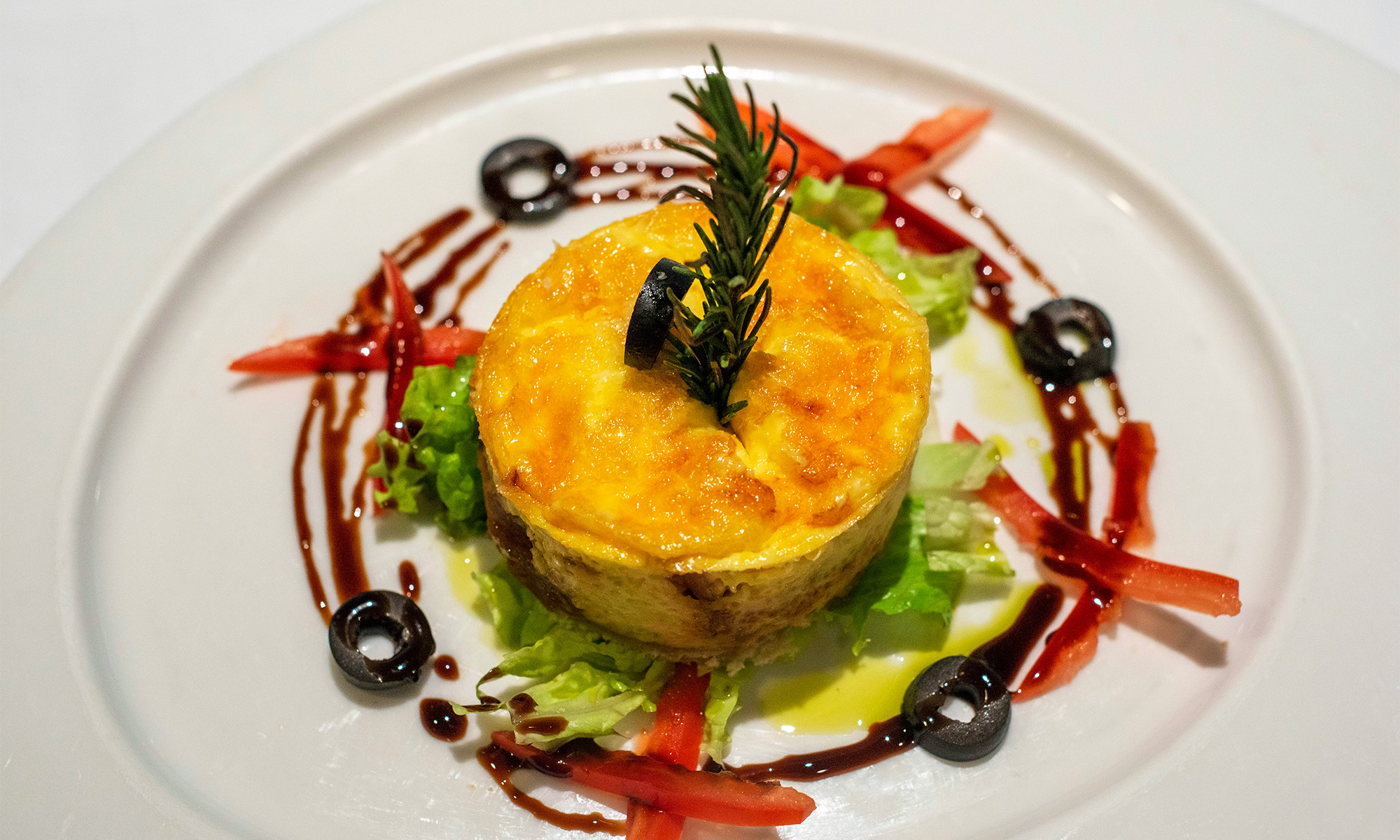 Quiche Eine Quiche in Form eines kleinen Törtchens auf einem Bett mit Salat, Paprika und Oliven.