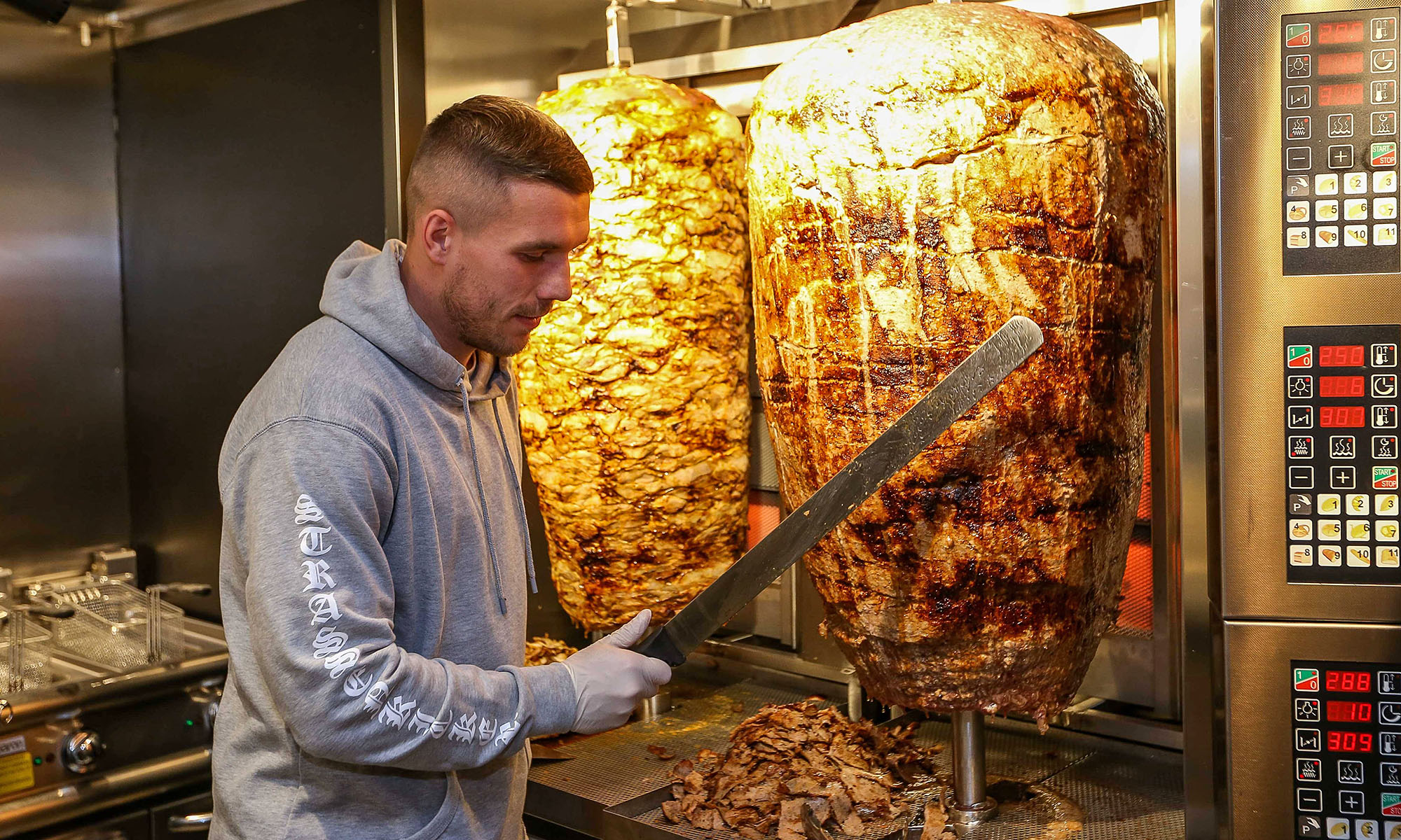 Lukas Podolski an einem Drehspieß für Döner in einem Imbiss