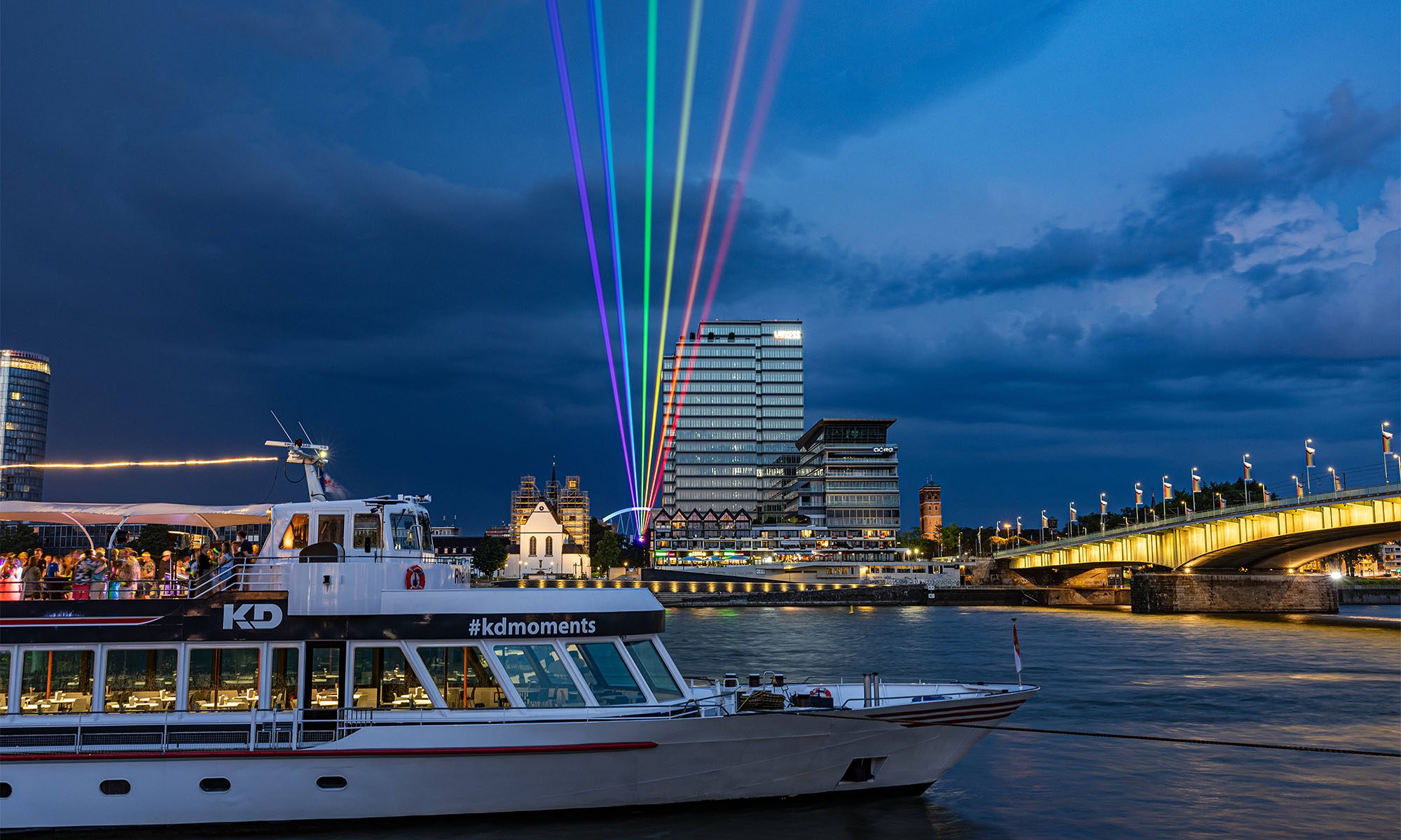 Ein Schiff der KD fährt nachts über den Rhein, im Hintergrund das Lanxess-Gebäude.
