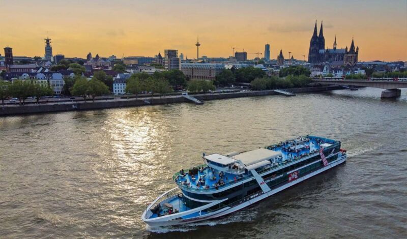 Ein Rheinschiff der Köln-Düsseldorfer fährt in der Abenddämmerung vor dem Kölner Altstadtpanorama auf dem Rhein